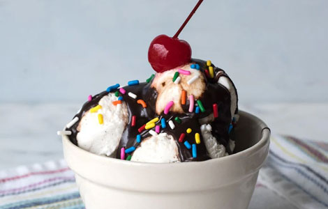 Vanilla ice cream topped with chocolate sauce, rainbow sprinkles, and a 
cherry in a white bowl at Cream Curls Dunfermline 
